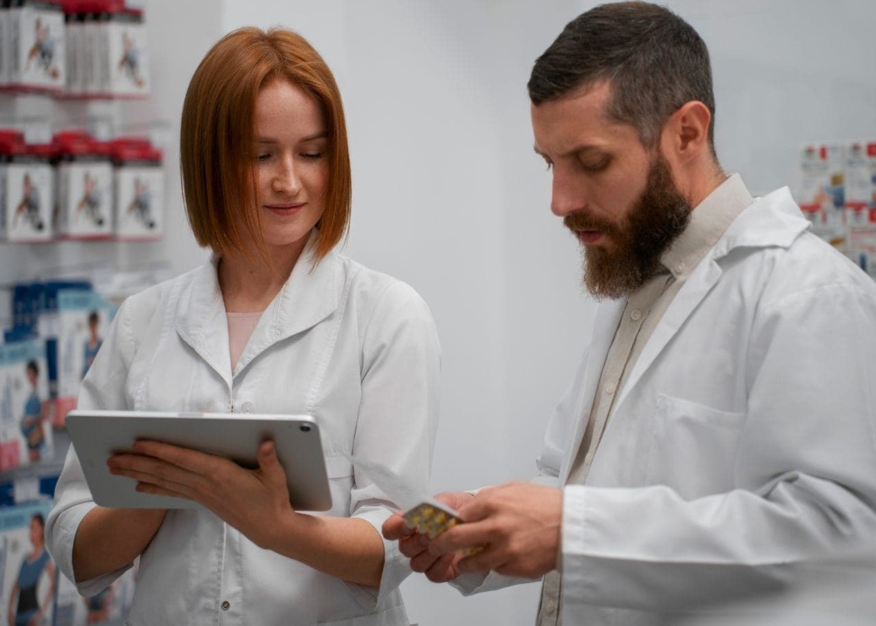 Female pharmacist training a male coworker with a tablet in the pharmacy